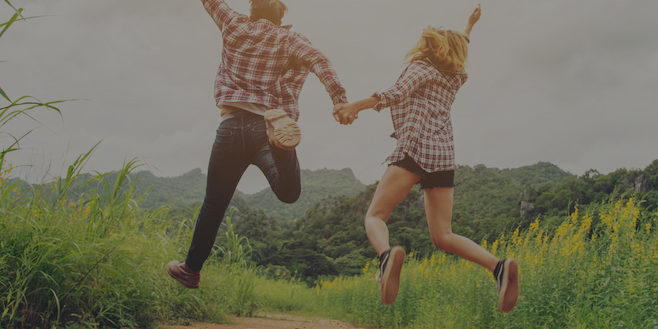 young hipster couple in love outdoor jumping at yellow flower field with mountain sunset background. jump up high enjoying freedom and enjoy.